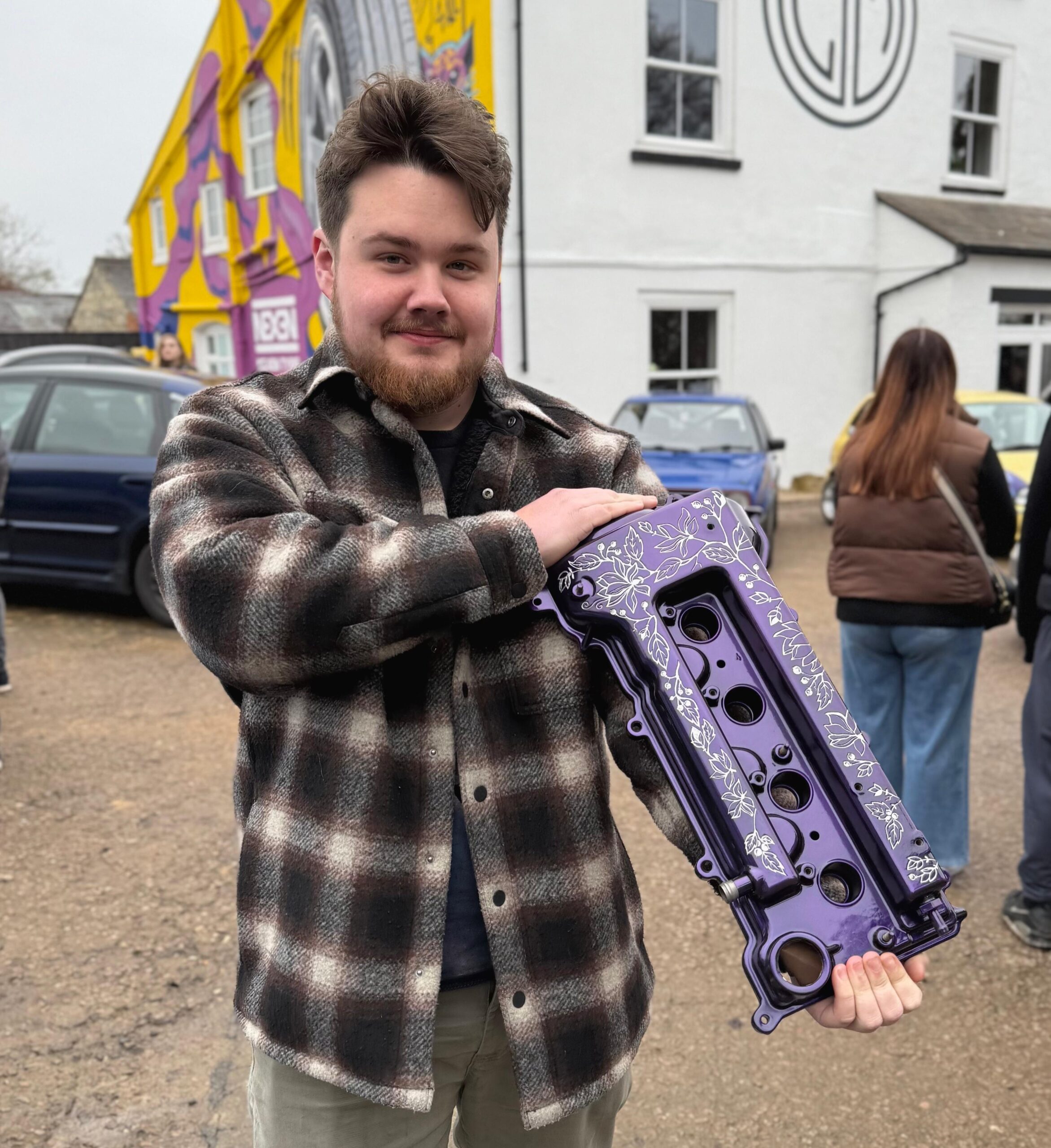 Happy customer Adam Shone Miso_MR2 olding a Toyota MR2 1ZZ engine cover that has been custom engraved with a floral design by JODEX Engravings, purple and silver colour